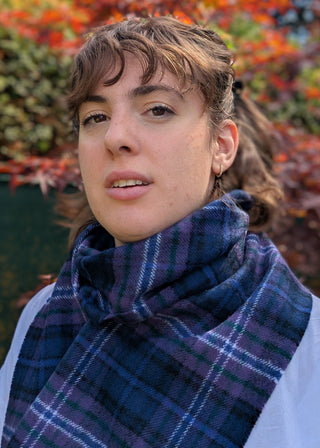 Zu sehen ist ein karierter Lammwollschal im Tartan Scotland forever. Vorherschend sind Violetttöne mit Akzenten in weiß, grün und blau