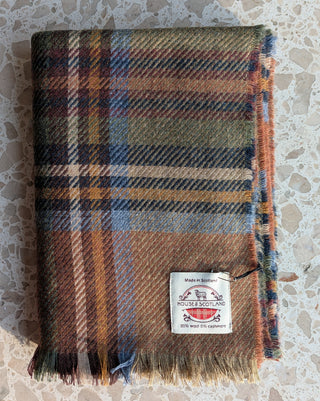 Der feiner karierter Schal aus Wolle und Kaschmir in den Farben beige, braun, blau und grün ist zusammengelegt. Gut erkennbar ist seine typische Fransenkante.